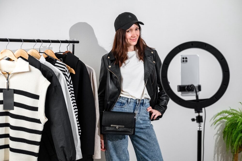 Fashion blogger recording vlog about clothes. Female blogger or stylist standing in front of camera showing clothes, filming vlog episode for her channel. Content creator concept.