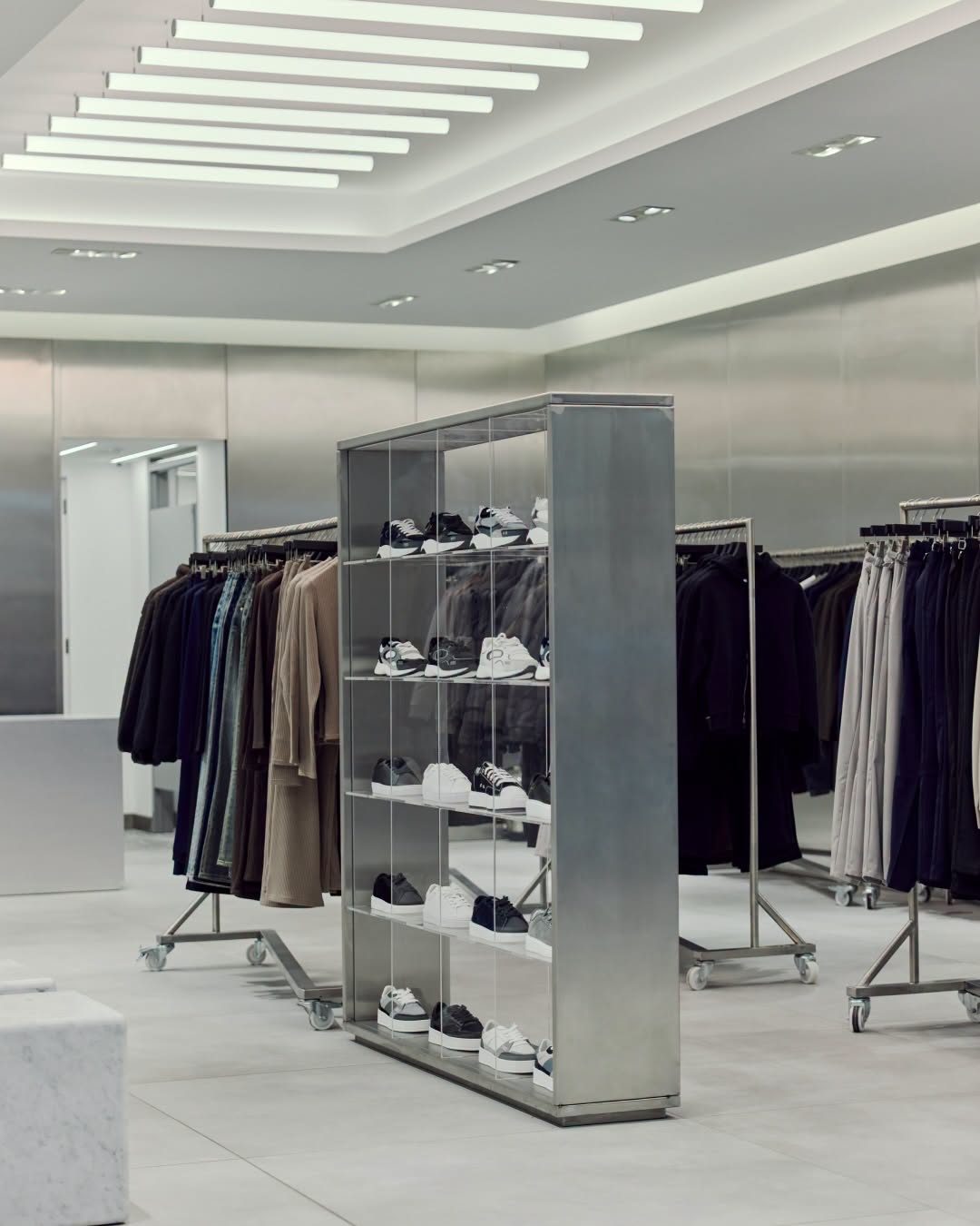 Clothing rails on wheels and a steel and acrylic trainer display beneath linear ceiling lights in the ARNE pop-up