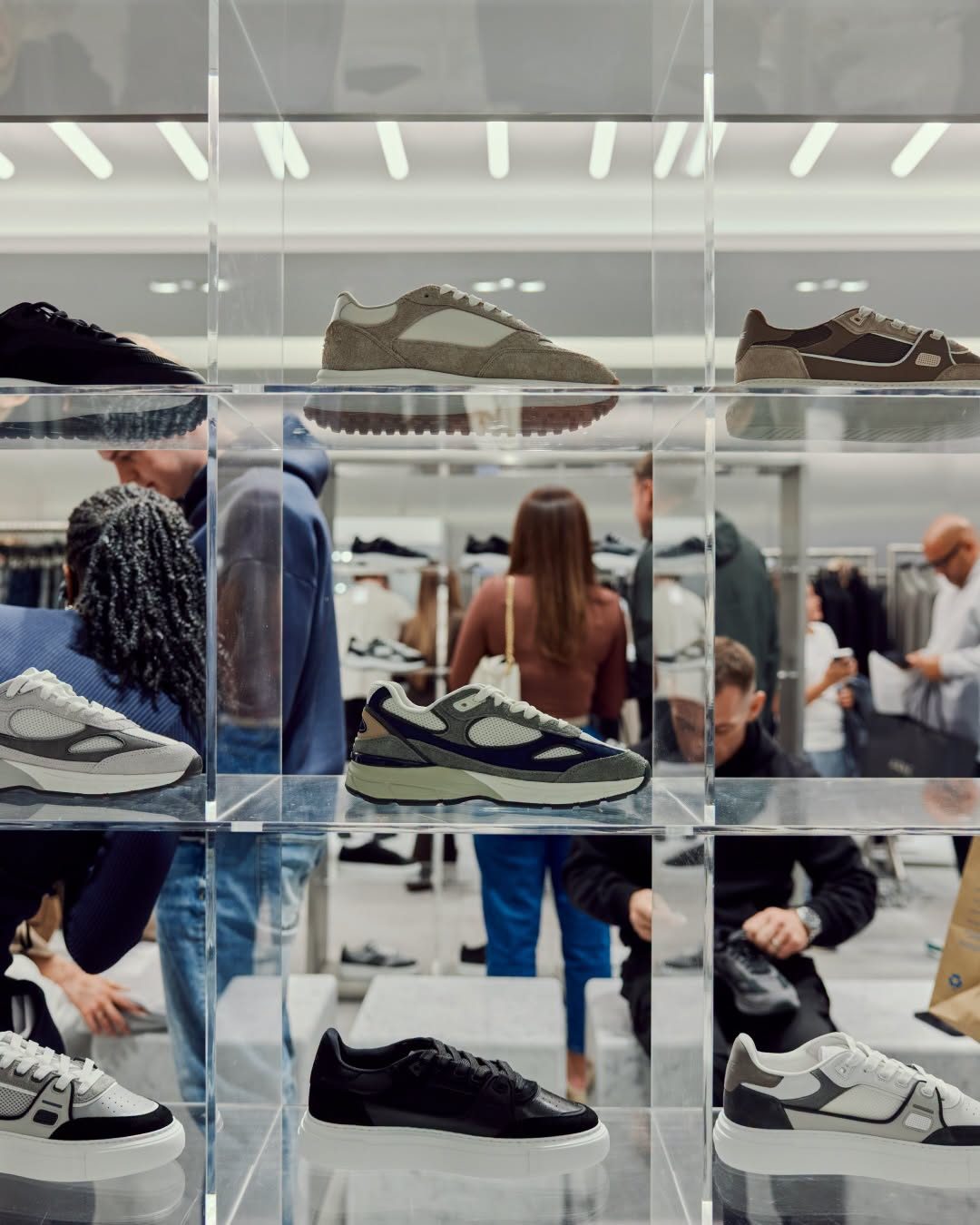 Trainers on acrylic shelves in the ARNE pop-up, with shoppers browsing behind