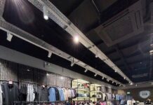 BADGE to Open Outlet Store at Dalton Park Designer menswear store interior with rails of jackets and knitwear on dark marble-effect plinths, herringbone wood flooring and track lighting