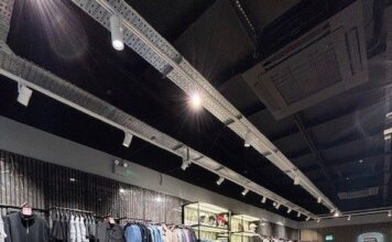 Designer menswear store interior with rails of jackets and knitwear on dark marble-effect plinths, herringbone wood flooring and track lighting