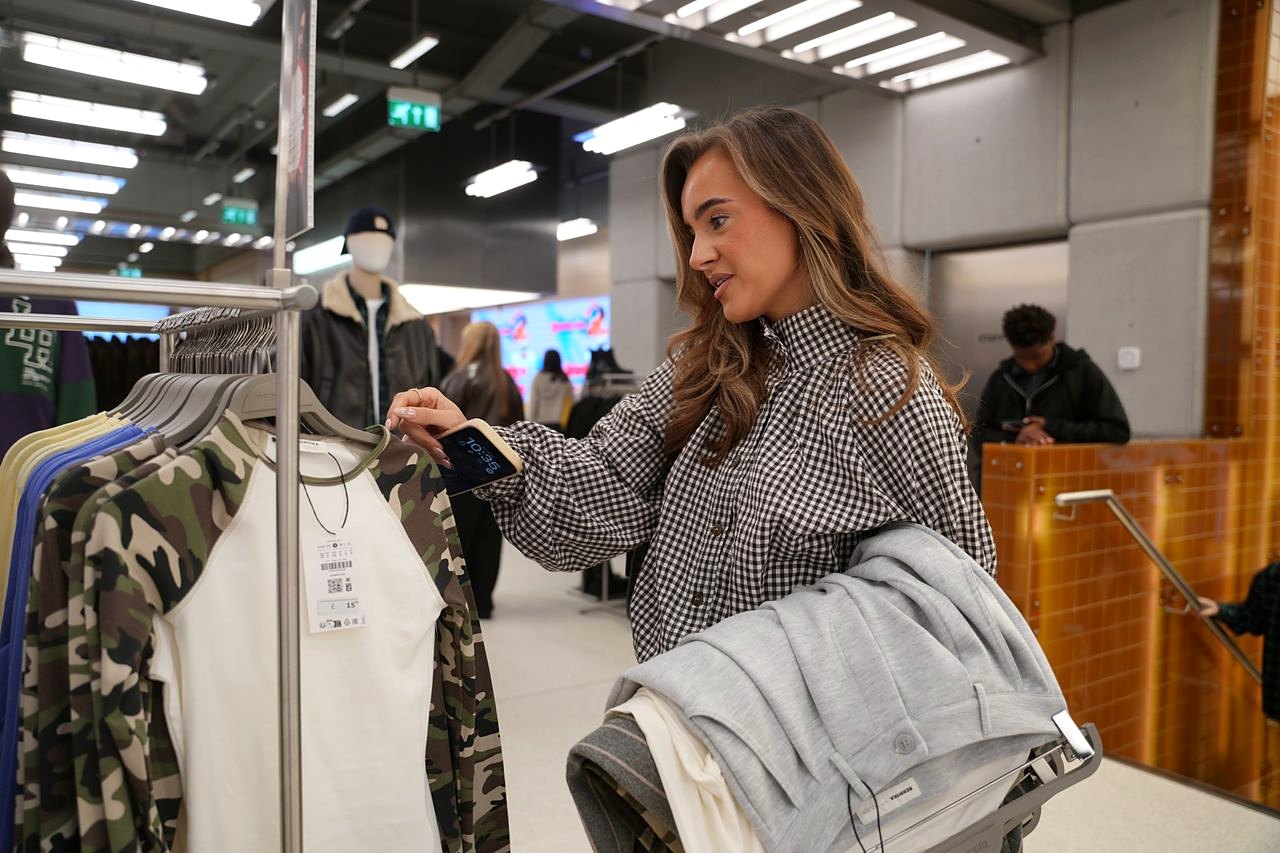 Shopper browsing camouflage and cream tops on a clothing rail inside the Bershka store at Westgate Oxford