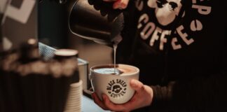 Barista pouring steamed milk into a Black Sheep Coffee branded cup at the counter
