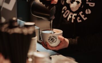 Barista pouring steamed milk into a Black Sheep Coffee branded cup at the counter