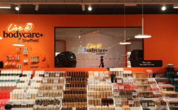 Bodycare & PMC Shortlisted in the Retail Technology Innovation Hub Awards for Bringing AI-First, Experience-Led Store Vision to Life The Live @ bodycare content studio at Bodycare Sheffield, seen through glass with a camera on a tripod, behind tiered make-up displays against an orange wall