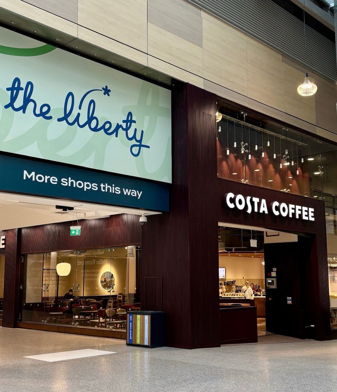 Costa Coffee entrance beside a The Liberty sign reading More shops this way, with seating visible through the glazing