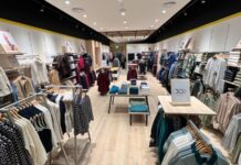 Interior of the Crew Clothing store at Westfield London, with knitwear, shirts and jackets on wall bays and rails either side of a central aisle