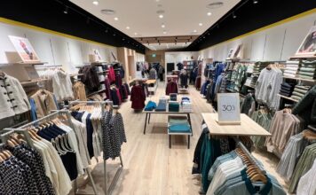 Interior of the Crew Clothing store at Westfield London, with knitwear, shirts and jackets on wall bays and rails either side of a central aisle