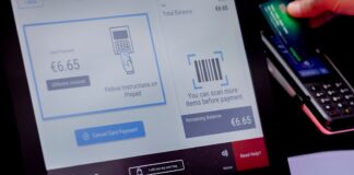 Self-checkout with a Toshiba screen showing a card payment, a red-lit barcode scanner and a shopper holding a card at the payment terminal