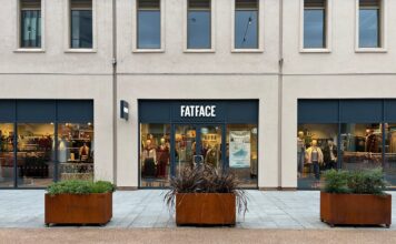 FatFace shopfront with a navy fascia and window displays of winter clothing, with planters on the paving outside