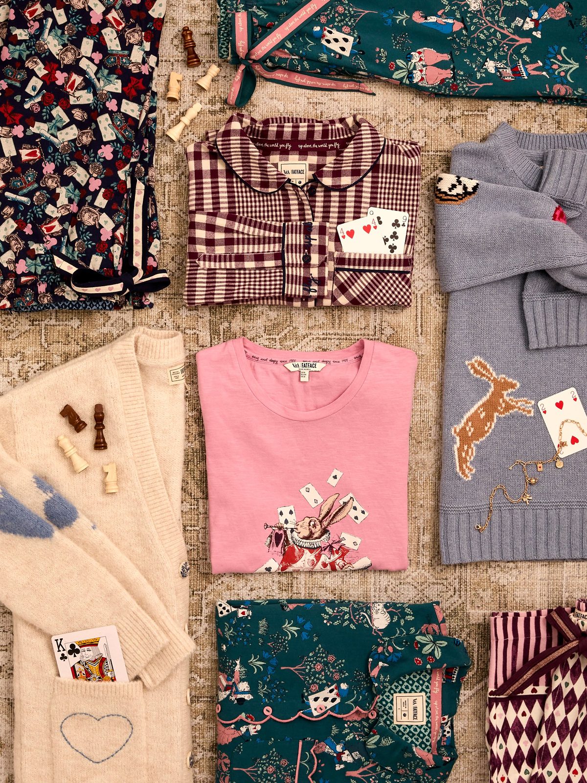 Flat lay of V&A | FatFace Wonderland pieces, including a checked pyjama shirt, a pink T-shirt with a rabbit print, a grey hare jumper and playing cards