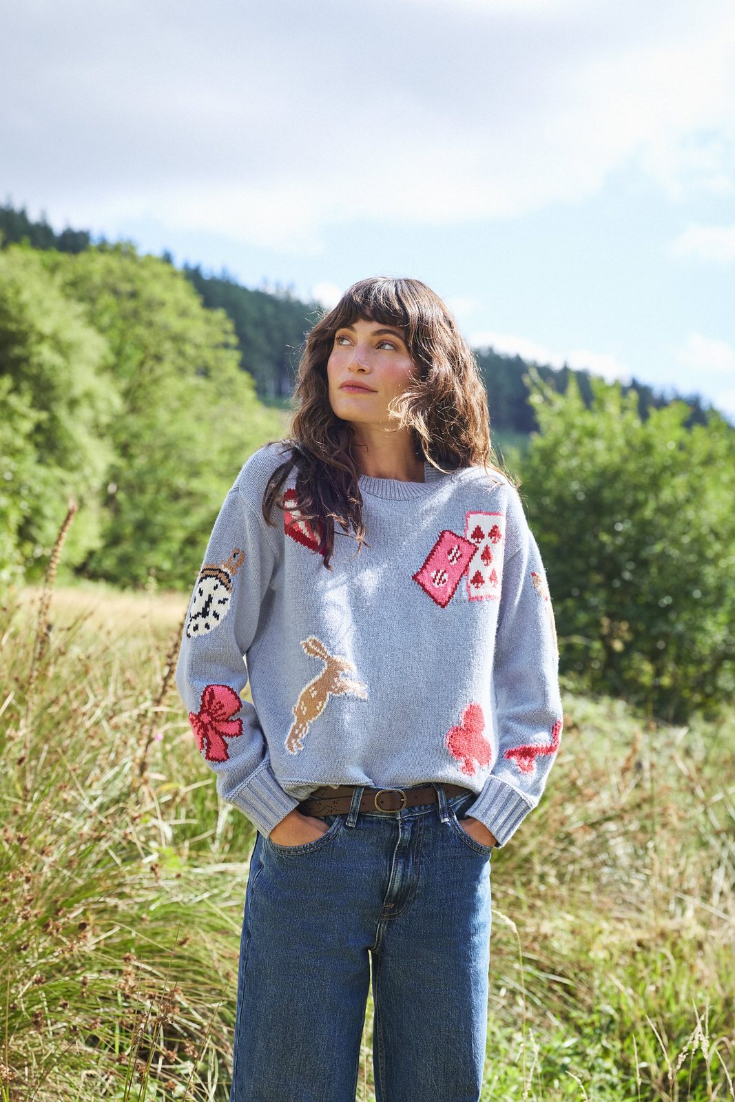 Model wearing a grey FatFace jumper with Wonderland motifs including a rabbit, playing cards and a pocket watch