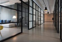 Modern office corridor lined with glass-walled meeting rooms, pendant lights and a lounge area