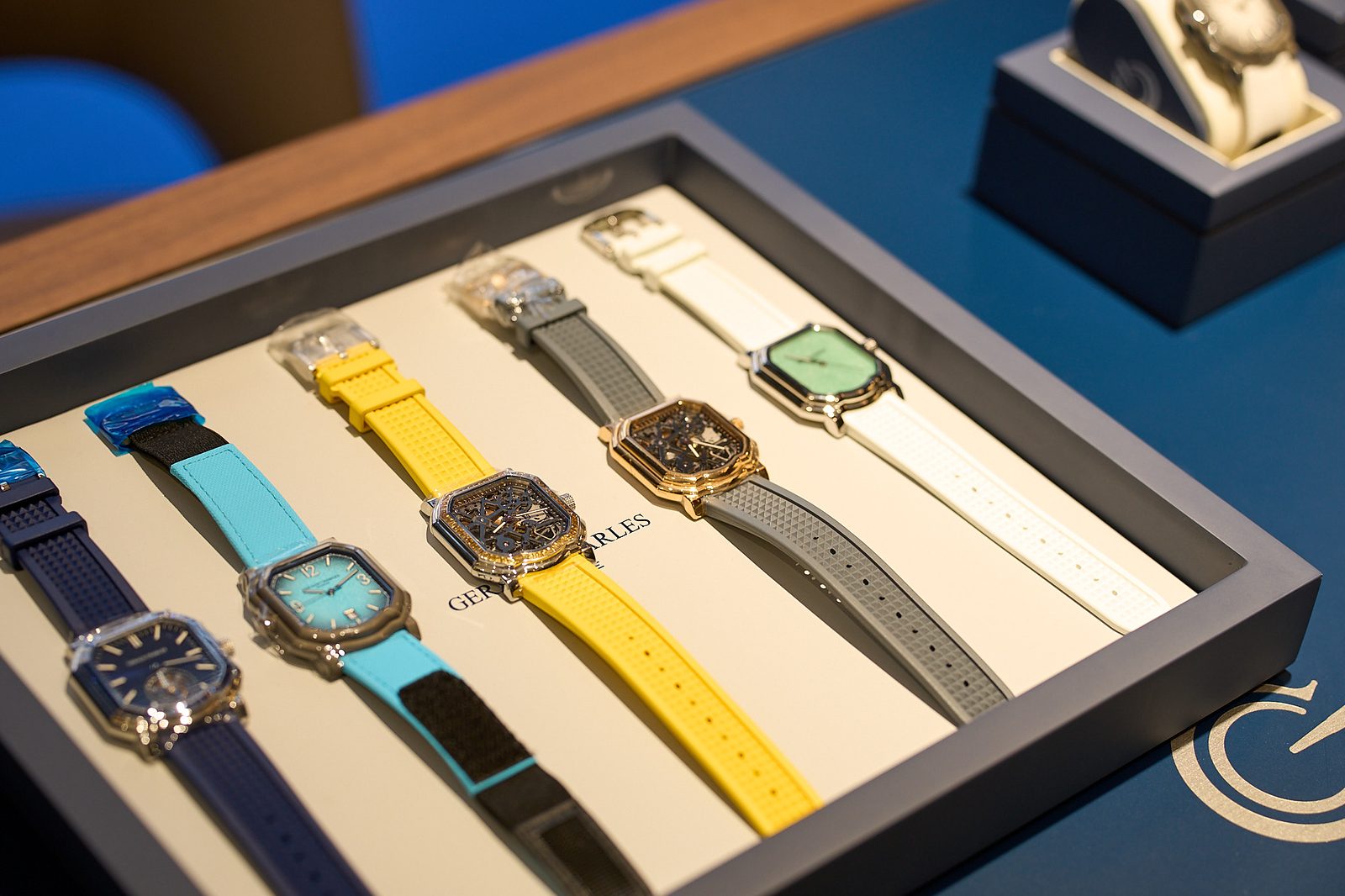 Tray of Gerald Charles watches with coloured rubber straps on a blue display counter