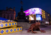 Giant chocolate frog sculpture beside an oversized open Chocolate Frog box at the Shaftesbury Memorial Fountain in Piccadilly Circus at night, with the illuminated screens behind