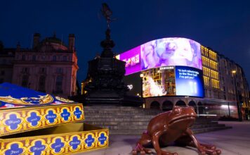 Giant chocolate frog sculpture beside an oversized open Chocolate Frog box at the Shaftesbury Memorial Fountain in Piccadilly Circus at night, with the illuminated screens behind