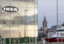 IKEA sign on the glass corner of a building in Aberdeen, with the harbour, a ship and a clock tower in the background