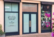 Shopfront of the forthcoming kate spade new york store at Cotswolds Designer Outlet, with window graphics announcing a November 2026 opening and a campaign image of pink shoes and a pink handbag