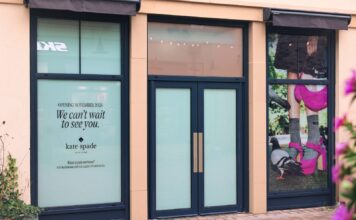 Shopfront of the forthcoming kate spade new york store at Cotswolds Designer Outlet, with window graphics announcing a November 2026 opening and a campaign image of pink shoes and a pink handbag