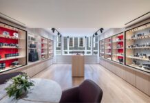 Room at Leica Store London Mayfair lined with red-backed glass cabinets of Leica cameras and lenses, with a central display plinth, bay windows and a marble table