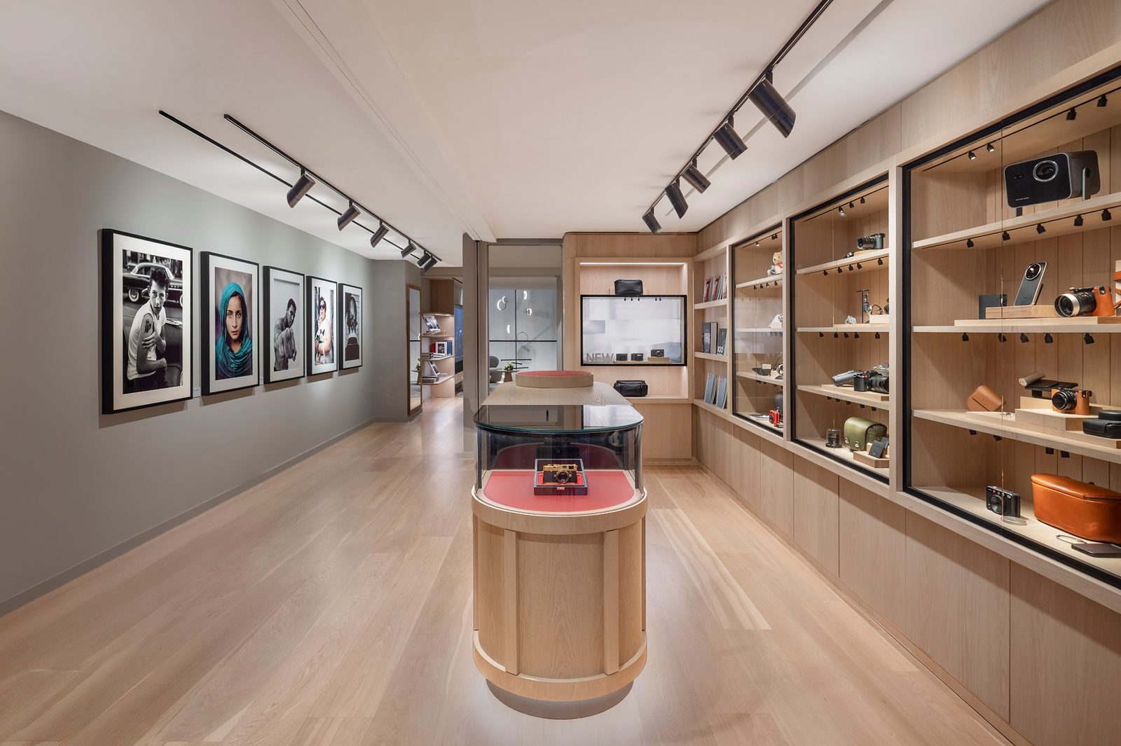 Ground floor of Leica Store London Mayfair with a wall of five framed photographs, a curved oak vitrine and glass cabinets of cameras and accessories