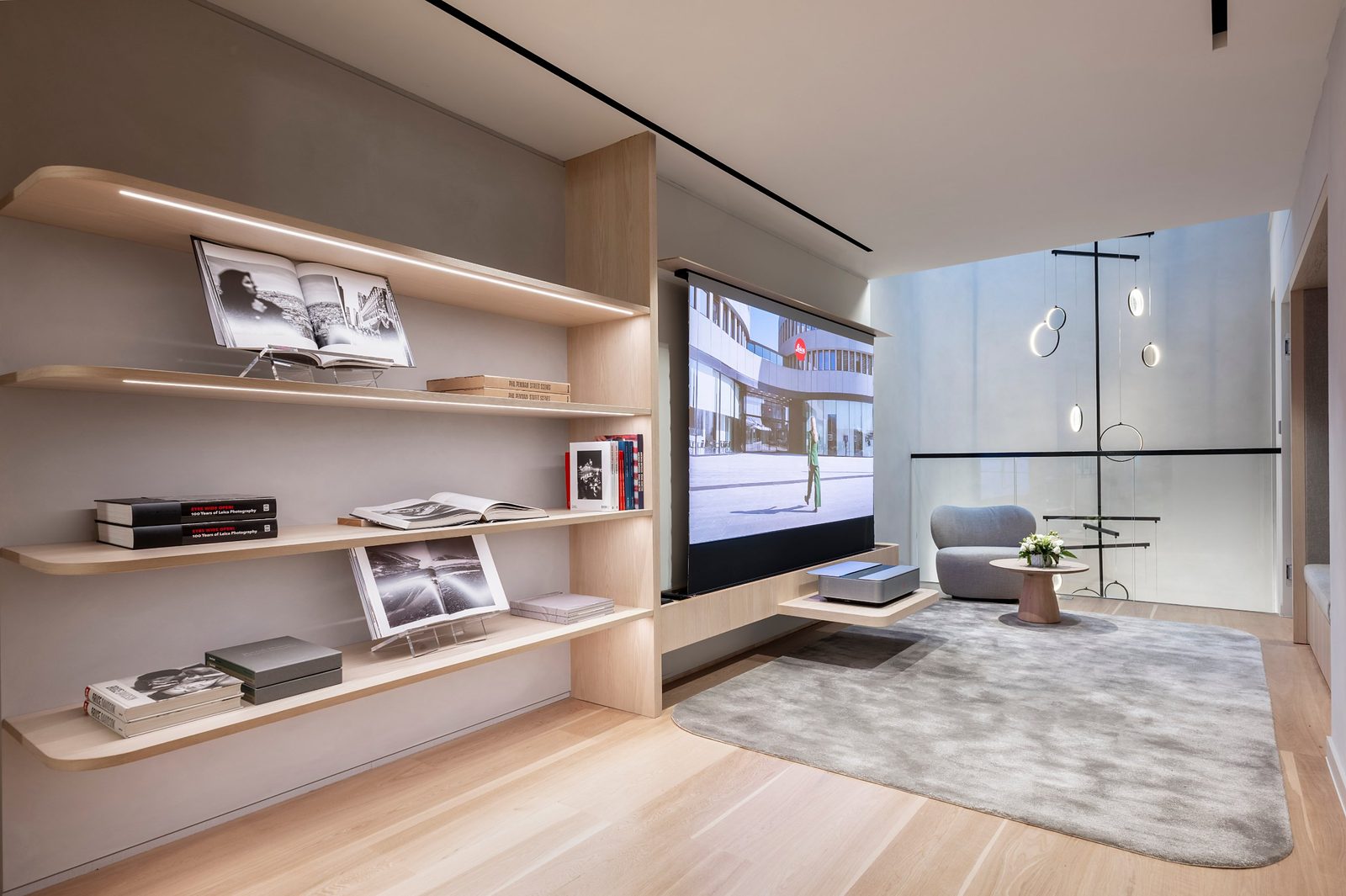Seating area beside the atrium at Leica Store London Mayfair, with shelves of photography books, a projection screen and a suspended ring light installation
