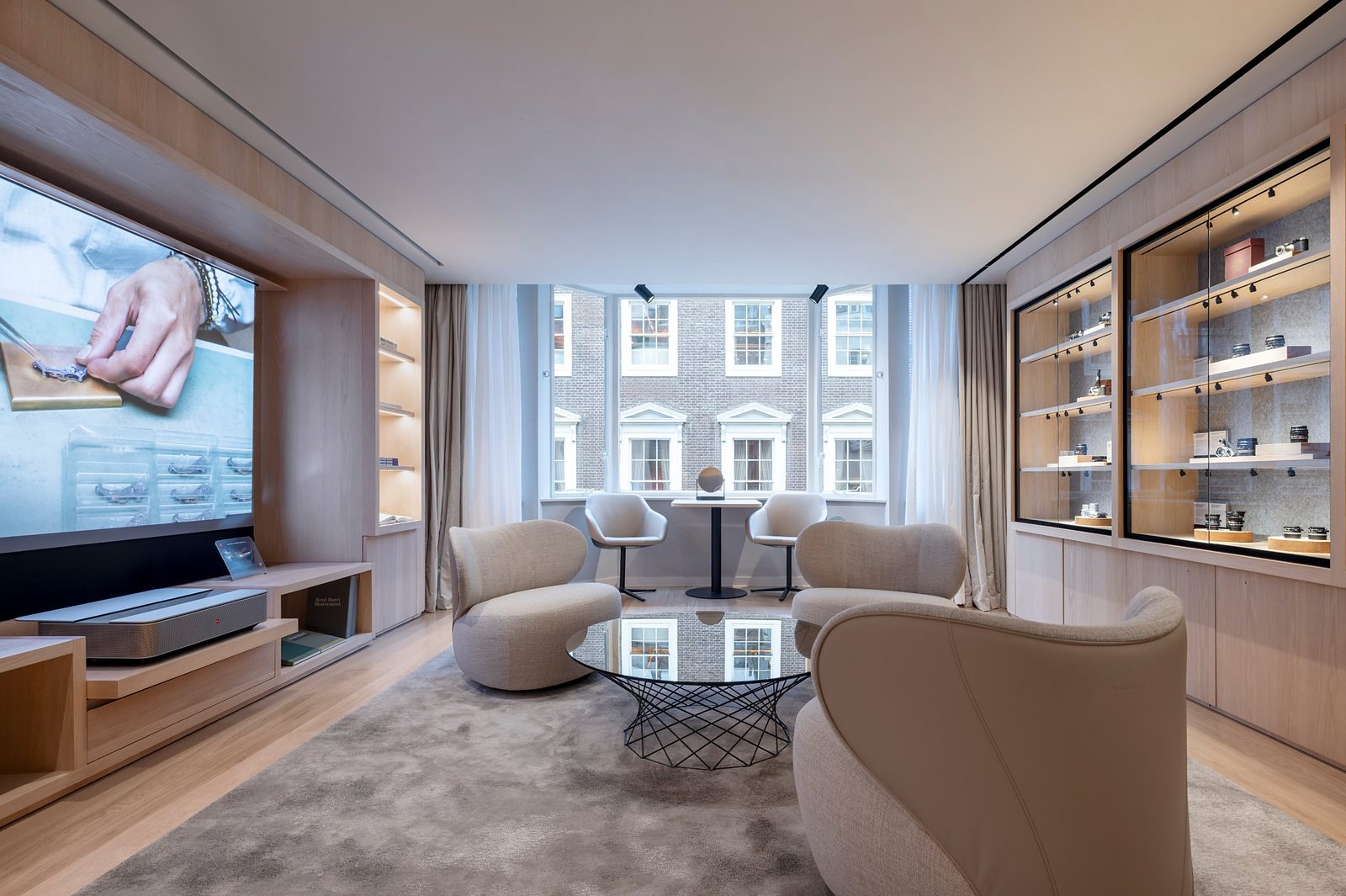 Lounge at Leica Store London Mayfair with a large projection screen, curved armchairs, a glass coffee table and display cabinets in front of a window bay