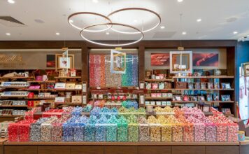 Lindt Chocolate Shop with a long Pick & Mix counter of LINDOR truffles sorted by colour, tubes of truffles on the back wall and three suspended ring lights