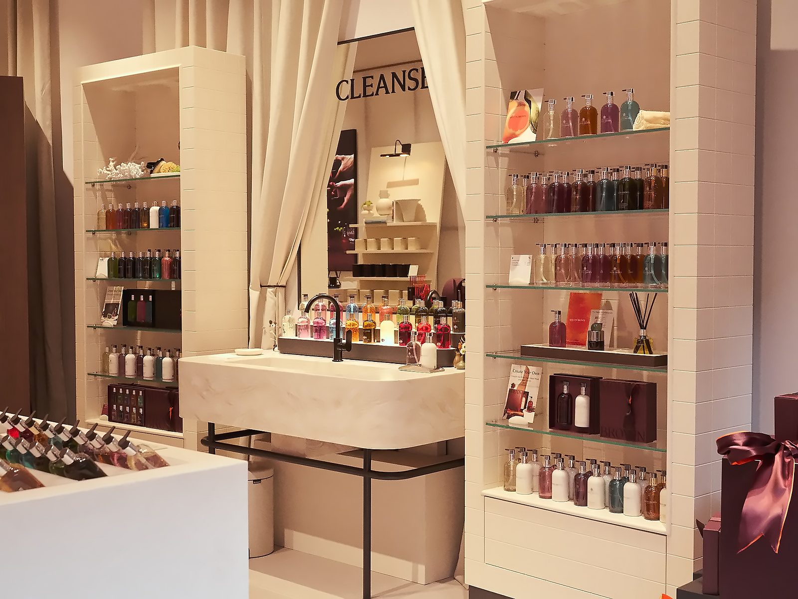 The Cleanse Bathroom with a basin, curtains and glass shelves of Molton Brown bath and body products
