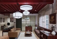 New Balance Opens Brand Hub at Arclight in Covent Garden Lounge at New Balance's Arclight brand hub with leather sofas, a coffee table, a glass display case and a wooden New Balance sign on an exposed brick wall beneath paper pendant lights