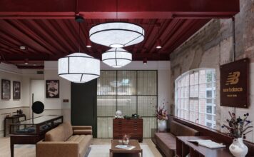 Lounge at New Balance's Arclight brand hub with leather sofas, a coffee table, a glass display case and a wooden New Balance sign on an exposed brick wall beneath paper pendant lights