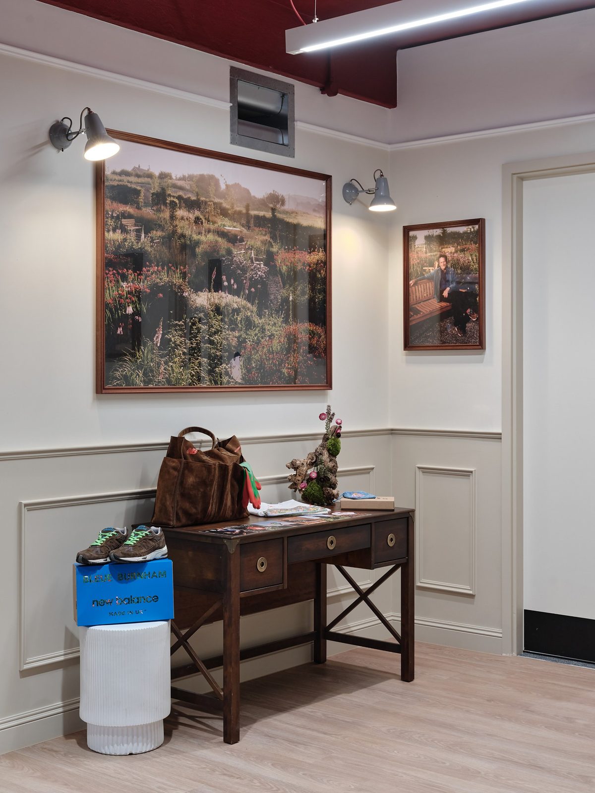 Entrance area with a wooden desk, a New Balance shoebox on a white pedestal and framed photographs on the wall