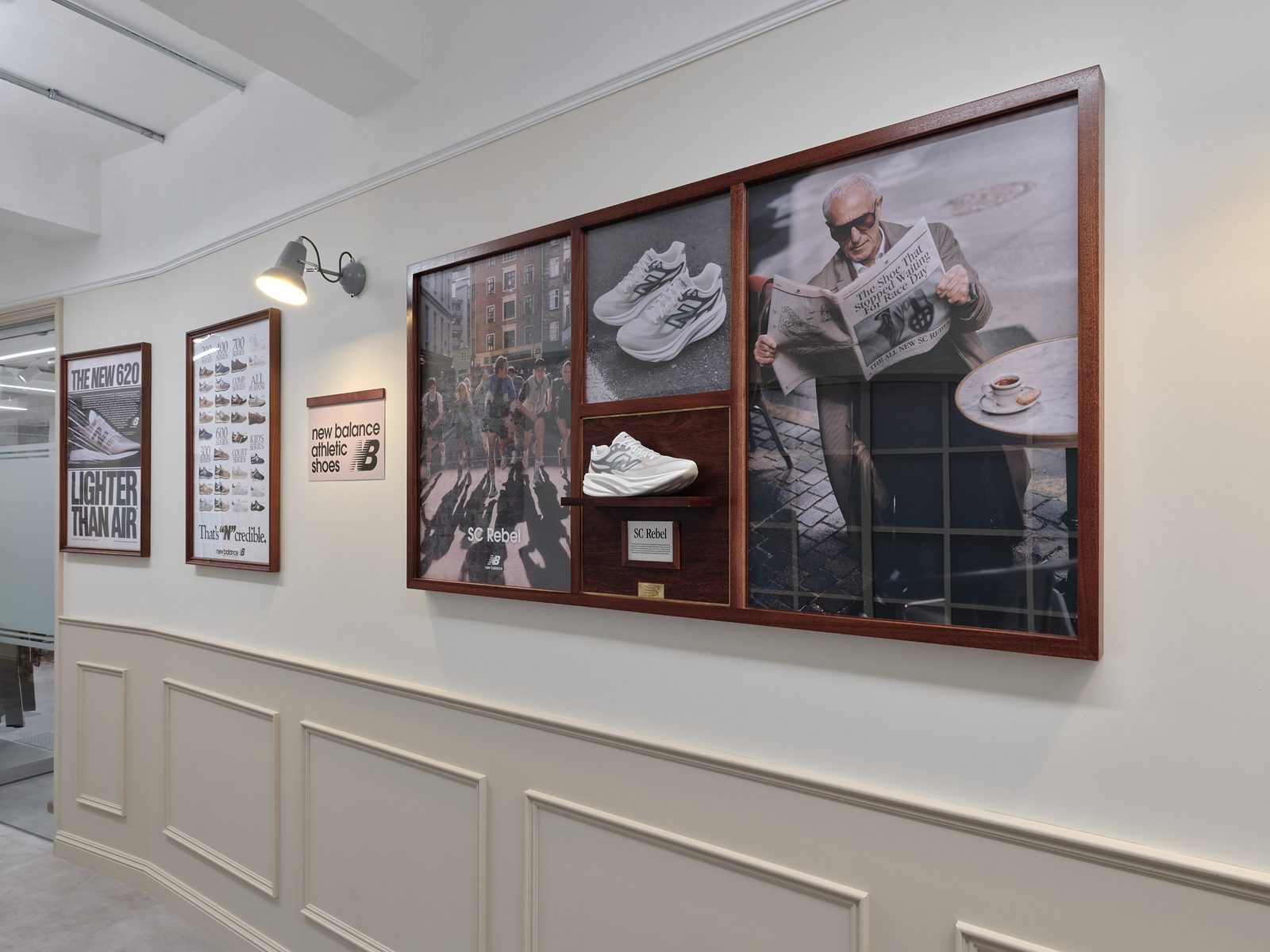 Wall of framed New Balance archive imagery and posters with trainers displayed on shelves inside the frames