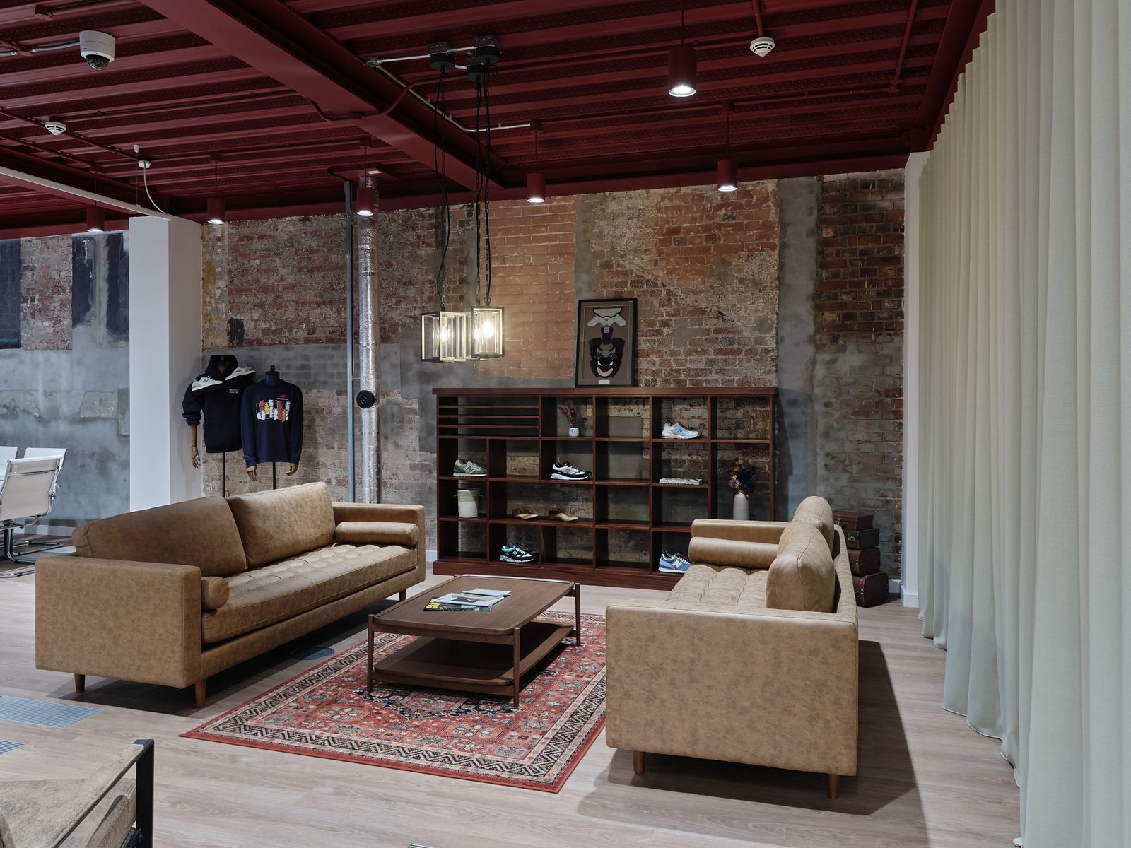 Lounge area with tan sofas around a coffee table on a patterned rug, with trainers on wooden shelving and New Balance apparel on display behind