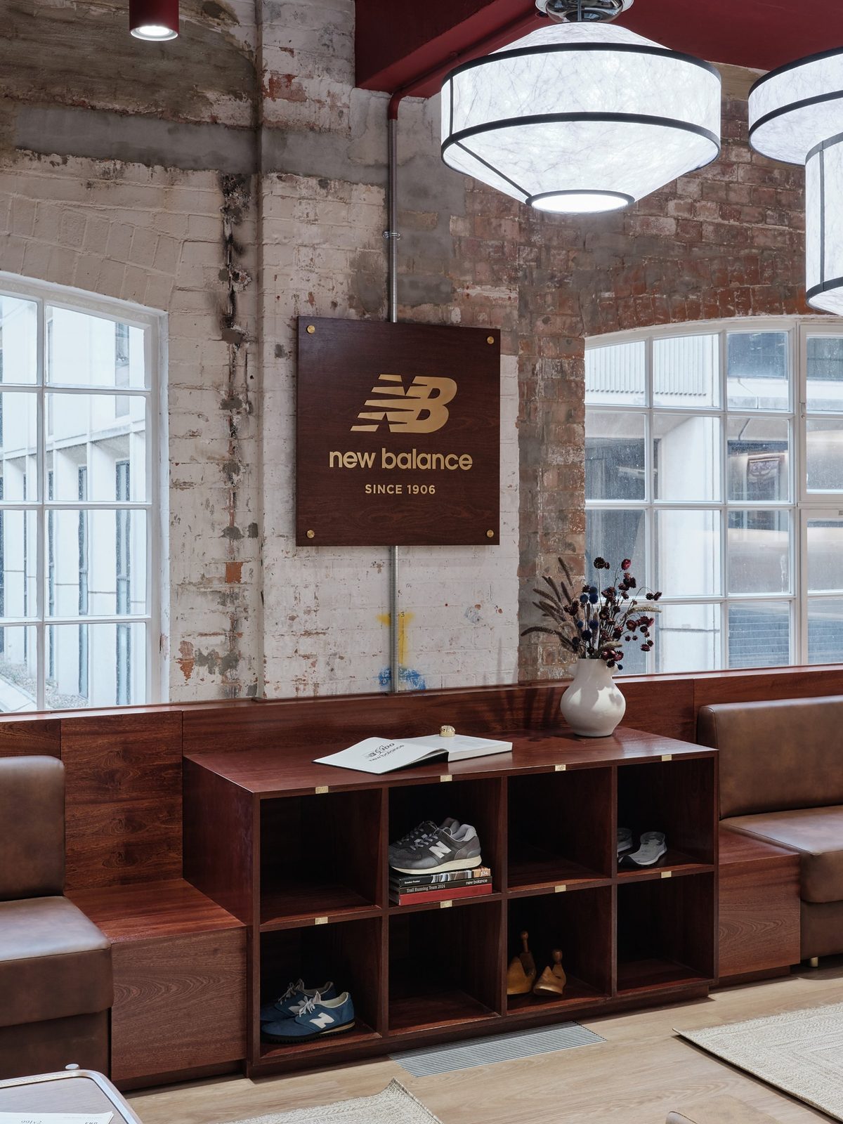 Wooden New Balance Since 1906 sign on a whitewashed brick wall above wooden cubbies holding trainers