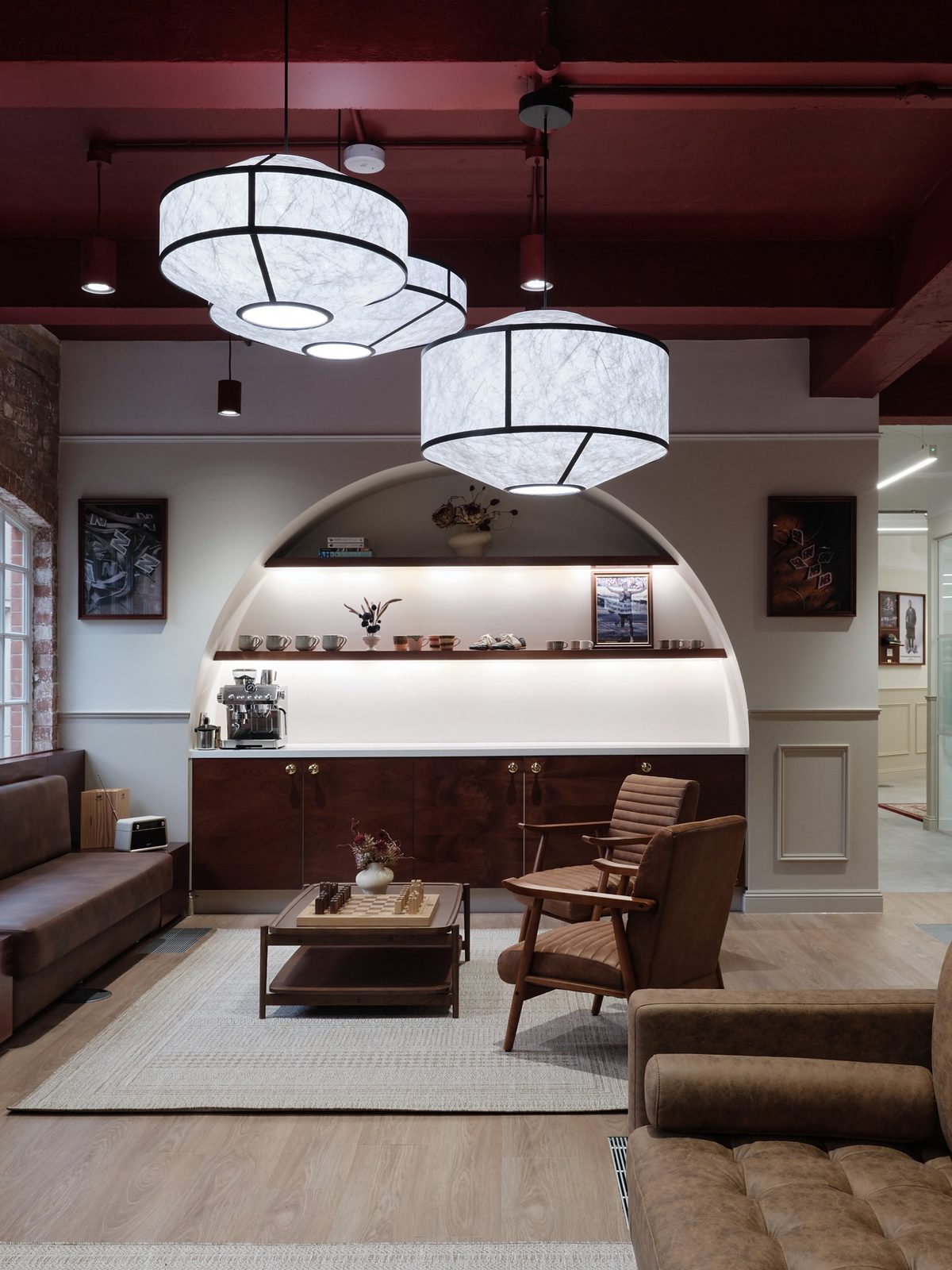 Lounge with an arched alcove of illuminated shelves holding mugs and trainers, leather armchairs and paper pendant lights
