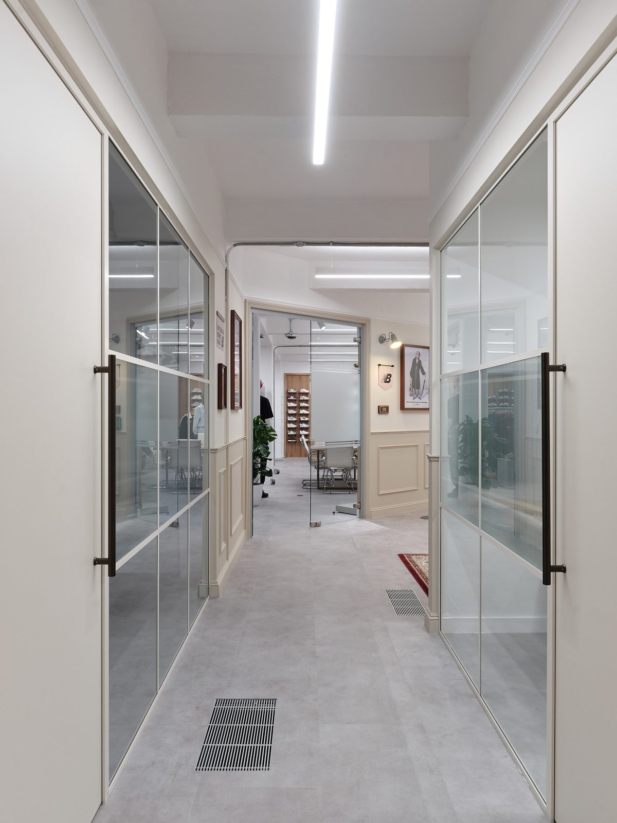 Corridor between glass-walled meeting rooms with panelled walls and framed New Balance imagery