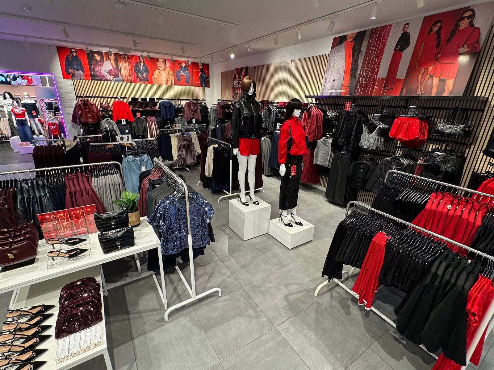 Inside the refurbished New Look store at Cribbs Causeway, with mannequins, rails of red and black partywear, an accessories table and campaign imagery above slatted wall panels