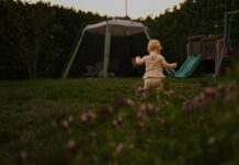 Young child walking across a garden lawn towards a slide and a play tent at dusk