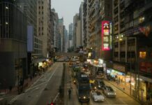 Busy Hong Kong street with buses and traffic between tall buildings, shops and illuminated vertical signs