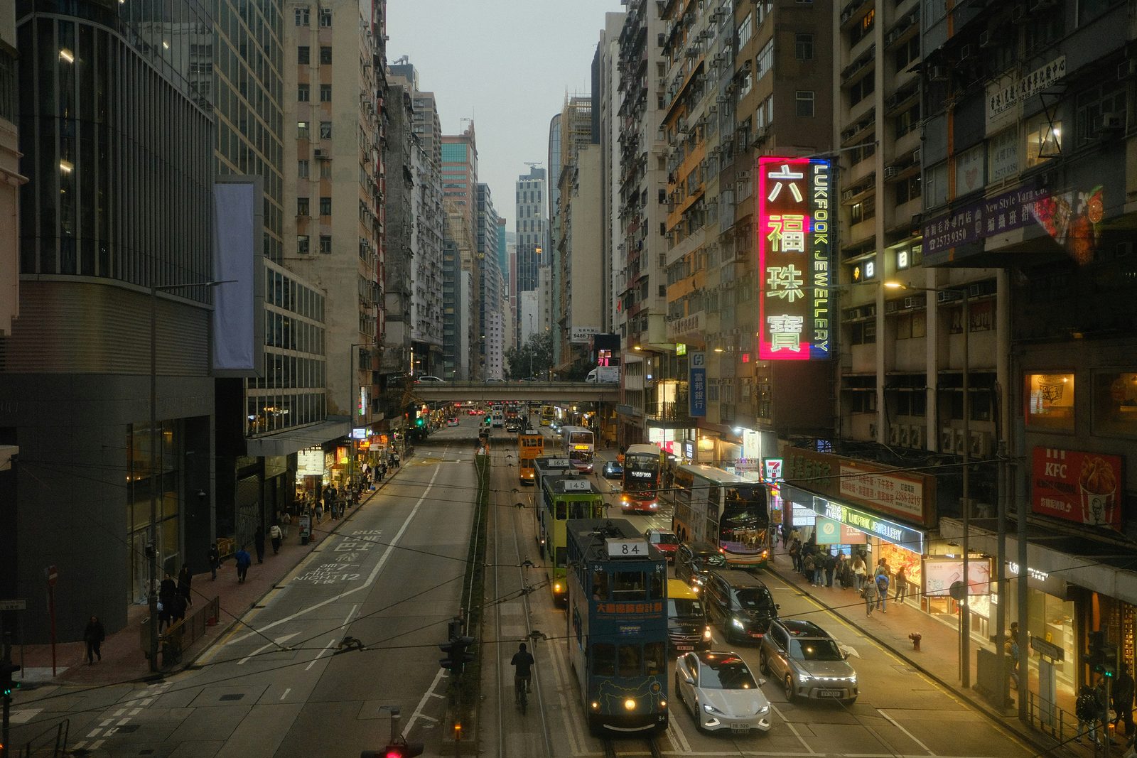 Busy Hong Kong street with buses and traffic between tall buildings, shops and illuminated vertical signs