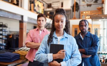 Three retail workers standing in a clothing shop, the woman in front holding a tablet
