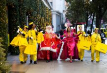 Selfridges Bellhops in yellow uniforms carrying yellow shopping bags walk along Oxford Street with Santa and the Showgirl