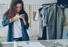 How Retailers Can Use Short-Form Visual Content to Engage Customers Online Woman using a smartphone to photograph clothes in a fashion studio, beside a rail of garments and a worktable of sketches