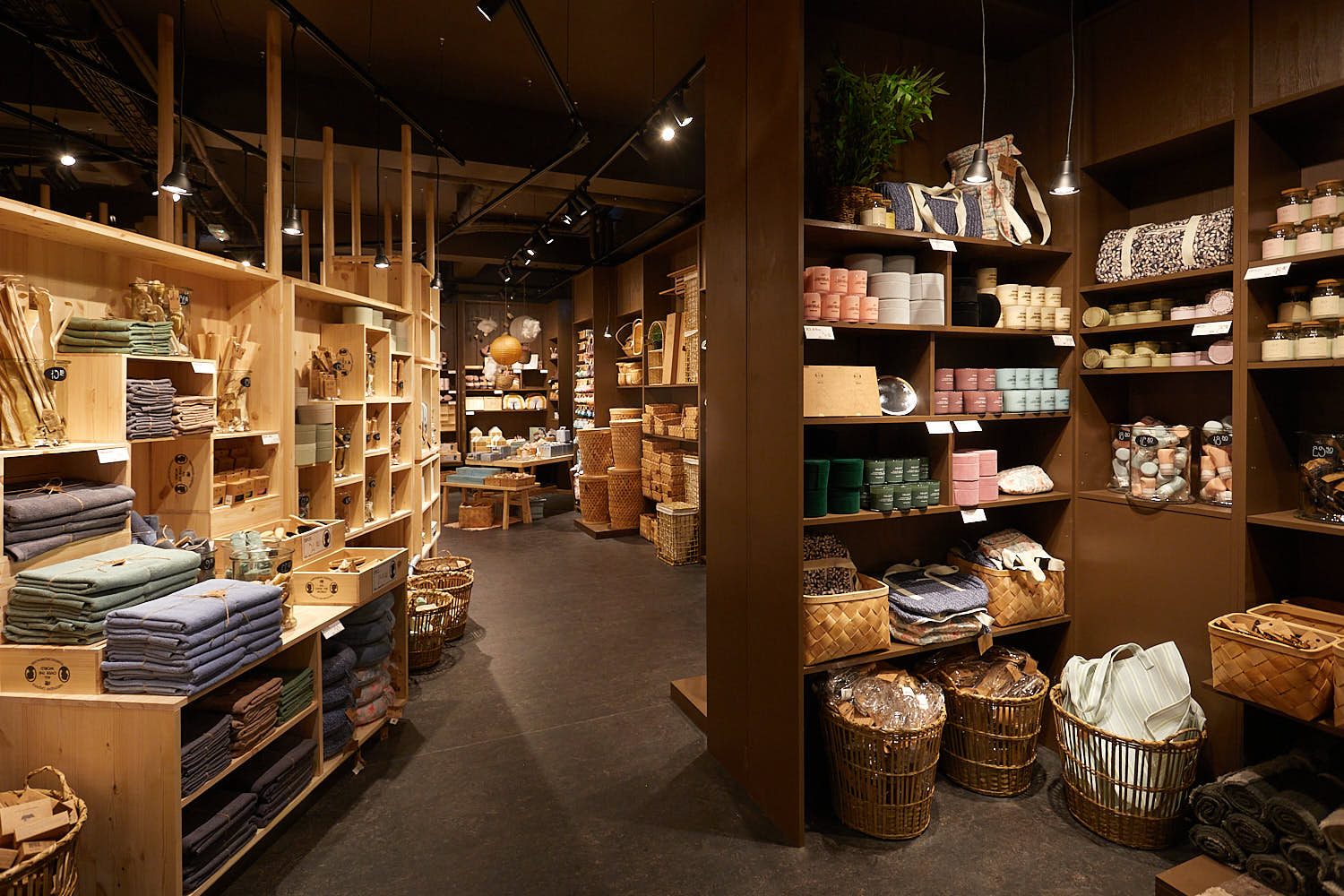 Søstrene Grene store interior with wooden shelving stacked with textiles, baskets, candles and storage boxes under pendant lights