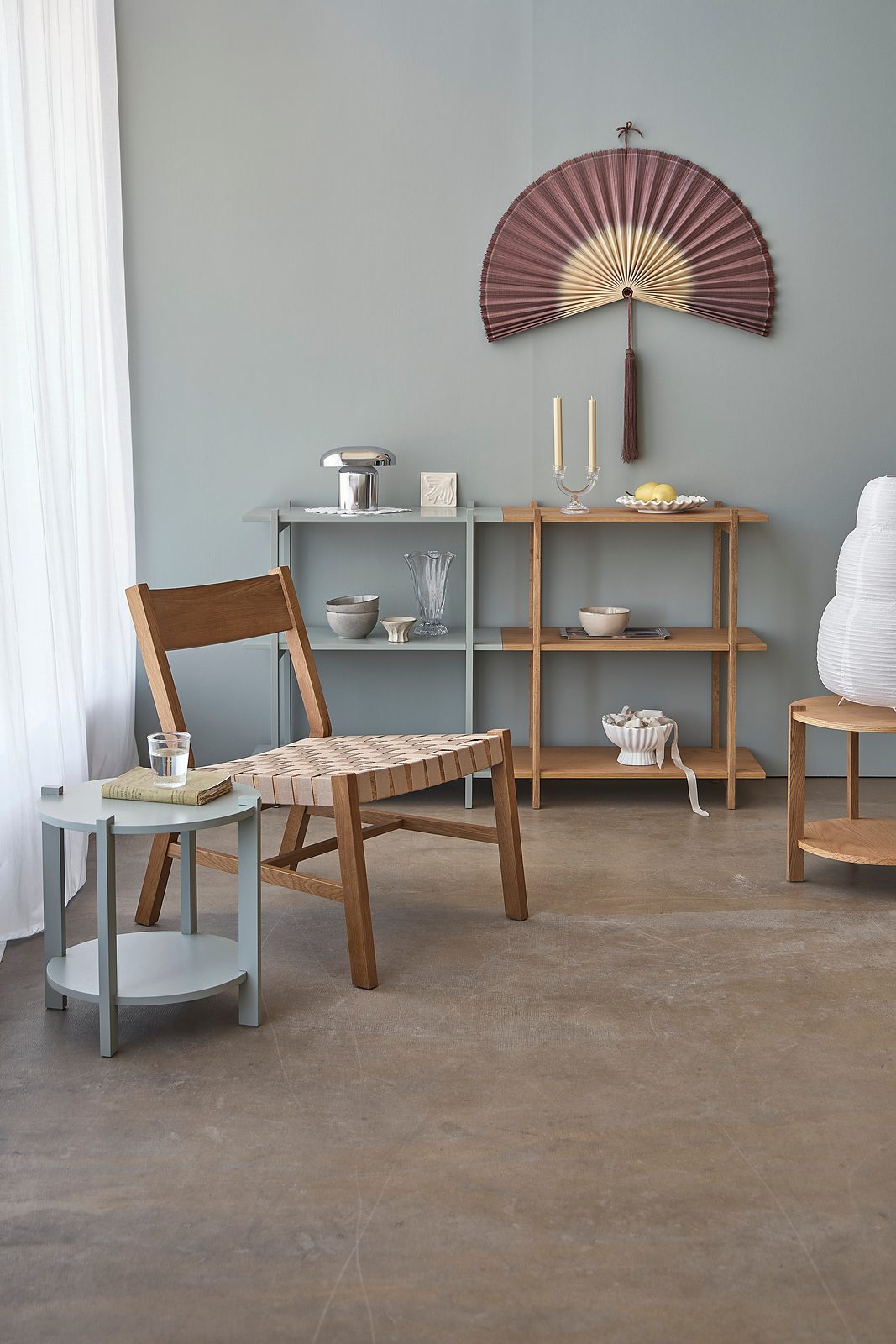 Søstrene Grene furniture collection with a wooden chair with woven seat, a side table and open shelving against a grey wall