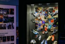 Display case of adidas football boots and balls in front of a collage of Chelsea FC memorabilia, beside a panel on Chelsea’s shirt sponsors