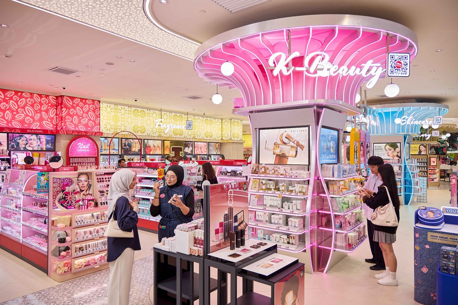 Pink illuminated K-Beauty zone at Watsons Plus, with a staff member helping a customer at a make-up display nearby