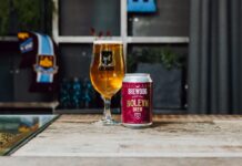 A can of BrewDog Boleyn Brew oat lager beside a full BrewDog glass on a wooden table, with a West Ham United scarf in the background
