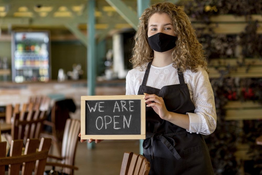 woman with mask holding chalkboard with open sign 1 Large
